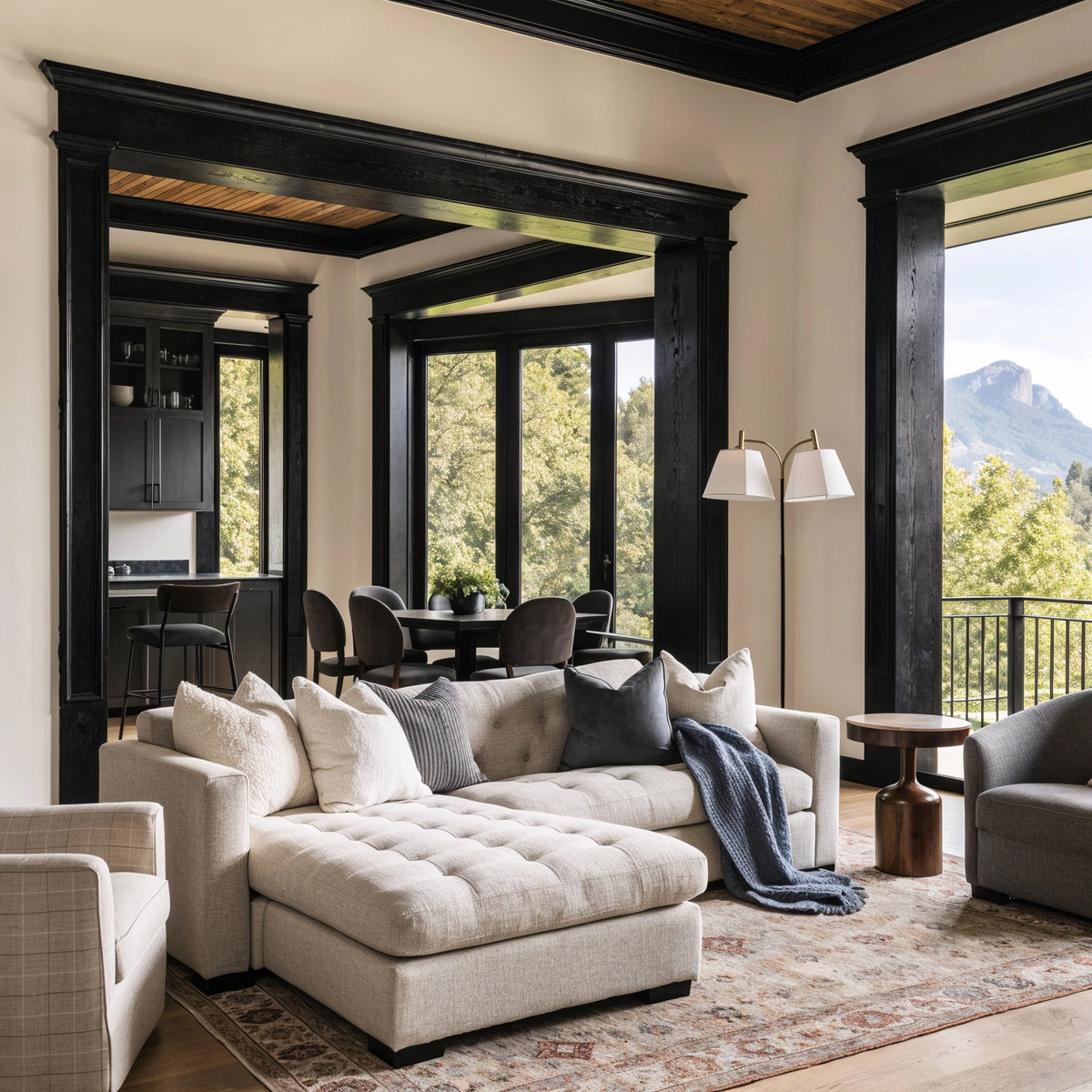 Black living room ideas with bold black architectural molding and doorway trim, cream sectional sofa, charcoal pillows, neutral rug, warm wood accents, and mountain views.