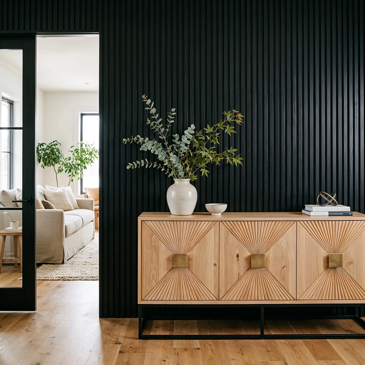Black living room ideas with floor-to-ceiling black slatted wall paneling, pale oak geometric credenza, neutral ceramic decor, greenery, and warm wood flooring.