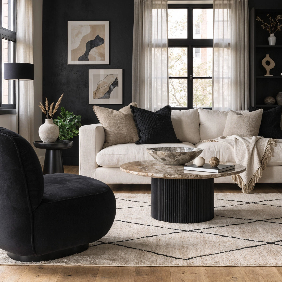 Black living room ideas with a deep black feature wall, cream sofa, beige textured pillows, black sculptural lounge chair, warm stone coffee table, sheer curtains, and neutral rug.