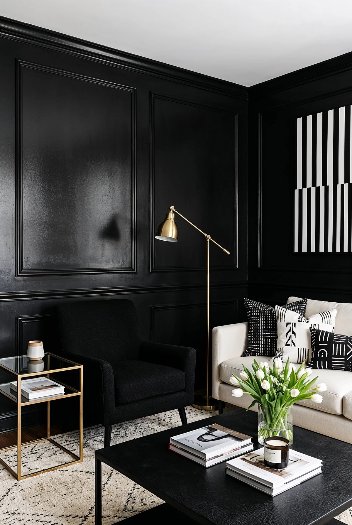 Black living room ideas with paneled black walls, cream sofa, black accent chair, black-and-white patterned pillows, brass floor lamp, and white tulips.