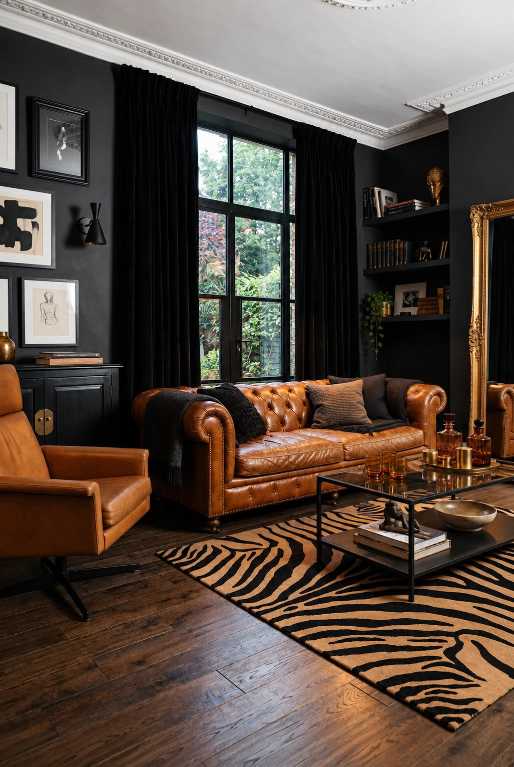 Black living room ideas with matte black walls, cognac leather Chesterfield sofa and lounge chair, caramel and black zebra rug, dark wood flooring, black curtains, built-in shelves, and gold mirror.
