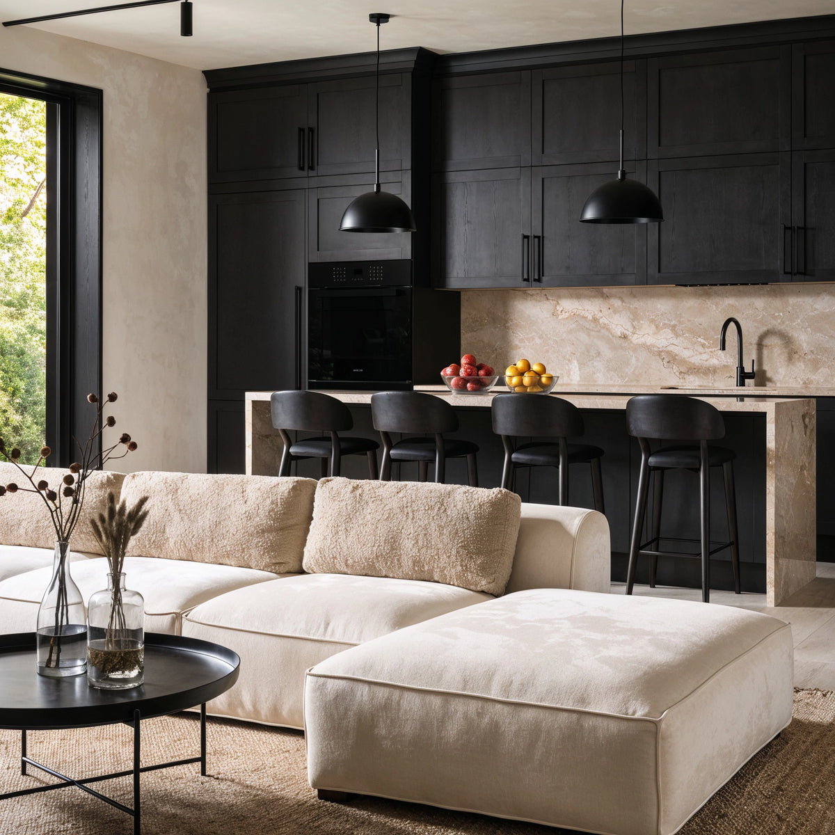 Black living room ideas with matte black kitchen cabinetry, cream sectional sofa, beige textured cushions, black pendant lights, warm stone counters, woven rug, and black coffee table.