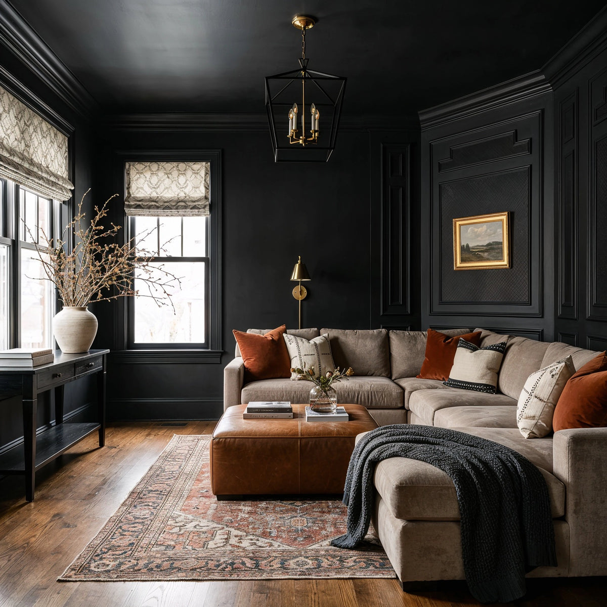 Black living room ideas with black paneled walls and ceiling, taupe sectional sofa, cognac leather ottoman, burnt orange pillows, and a traditional patterned rug.