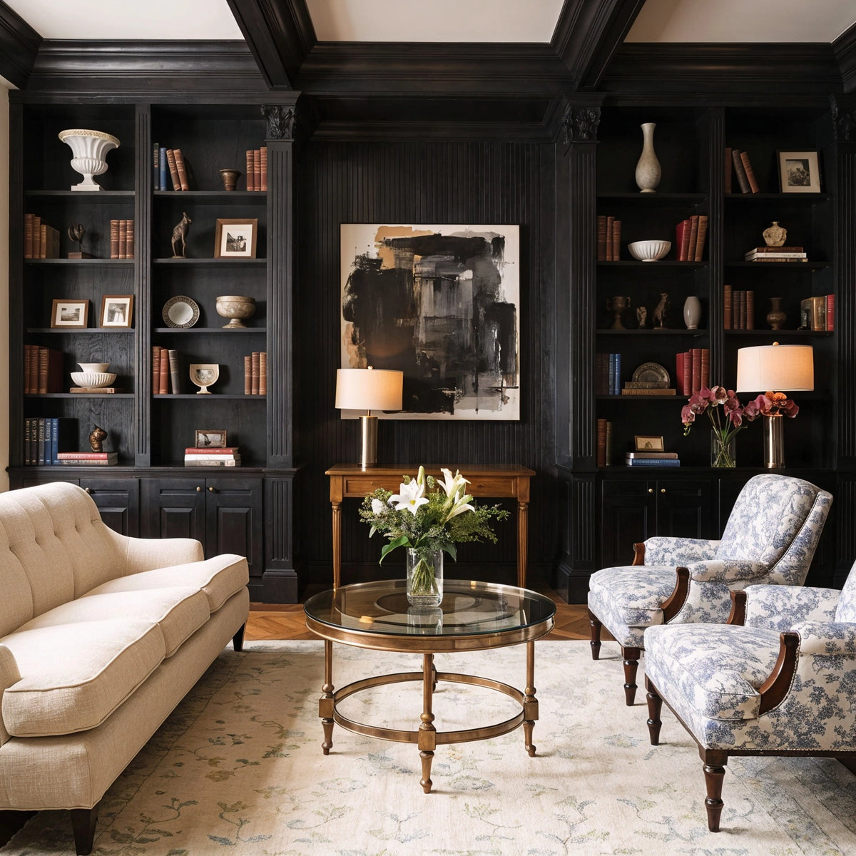 Black living room ideas with traditional black built-in shelving, classical millwork, cream sofa, blue patterned armchairs, brass glass coffee table, books, and collected decor.