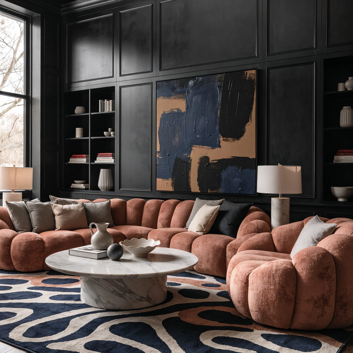 Black paneled living room with muted terracotta curved sectional and lounge chair, round white marble coffee table, abstract wall art, and navy cream patterned rug.