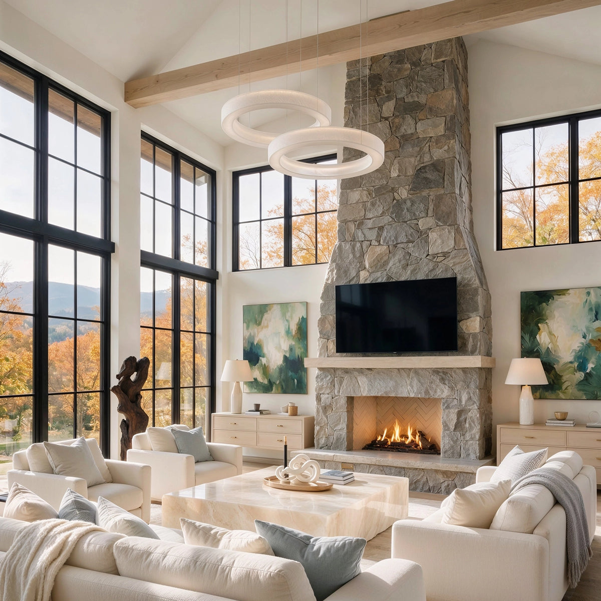 Bright beige living room with natural light, black-framed windows, cream sofas, blue-gray accents, a stone fireplace, wood beam, and glass ring chandeliers by CharmyDecor
