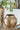 Gold metallic vase with green floral arrangement on a glass table
