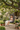 Child sitting in a hanging chair in a garden setting with plants and a house in the background.