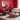 CharmyDecor red and beige living room with a red leather accent chair, cream sofa, woven round ottoman, floral rug, red paneled walls, and decorative branches.