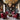 CharmyDecor red leather accent chairs in a sophisticated red and black living room with dark built-in shelves, brass coffee table, crystal chandelier, and abstract wall art.