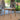 Charmydecor square acacia wood outdoor dining table in teak finish on a covered patio with garden background