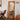 Irregular wavy framed mirror reflecting natural decor and wooden dining chairs