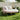 Round outdoor daybed with white cushions and a blanket in a garden setting.