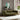 Green sofa in a living room with a painting and plants on a wooden side table.