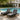 Two Charmydecor black acacia wood patio chaise lounges with dark gray cushions styled beside a swimming pool